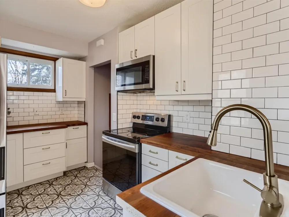 The same kitchen after renovation — white shaker cabinets, subway tile, butcher-block counters and a new range